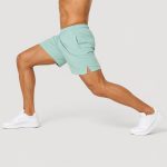 Male athlete wearing mint green workout shorts performing lunge pose, dynamic side profile, white sneakers