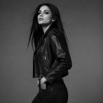 Women's black leather biker jacket model side profile B&W studio, asymmetric zip, notched lapel, twin diagonal zip pockets visible, zip cuffs