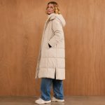 Women's cream longline puffer jacket model side profile, full zip, hood, side slit visible