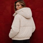 Women's cream puffer jacket model back view against burgundy backdrop, oversized hood, clean rear construction, elasticated hem
