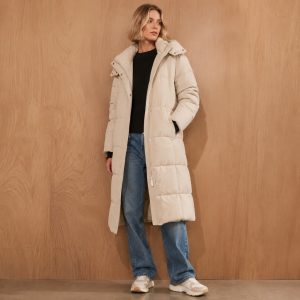 Women's cream longline puffer jacket model front view, full zip, drawcord hood with collar overlay, twin concealed hand pockets, side slits, mid-thigh length