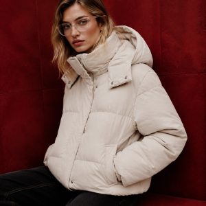 Women's cream puffer jacket model front view against burgundy backdrop, oversized hood, snap-button front, twin welt hand pockets, elasticated hem, cropped fit