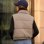 Women's taupe puffer vest model back view with navy cap, stand collar, clean rear construction, drawcord hem