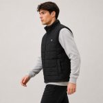 Men's black quilted vest model side profile walking, full zip stand collar, side pockets