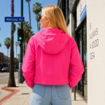 Women's hot pink windbreaker hoodie model back view, clean rear construction, elasticated hem