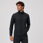 Back three-quarter view of male model wearing black mock-neck athletic jacket, clean back panel, ribbed cuffs and hem, paired with gray sweatpants, light gray backdrop