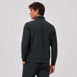 Male model wearing black mock-neck full-zip athletic jacket with hands in side pockets, ribbed hem and ribbed cuffs, set-in sleeves, paired with gray sweatpants, light gray backdrop