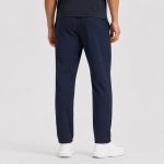 Back view of male model wearing navy athletic workout pants, straight leg, side pockets, white sneakers, dark t-shirt, light gray studio backdrop