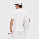 Back three-quarter view of male model wearing white polo workout shirt, back yoke visible, side vents at hem, white cap, white backpack over one shoulder, light gray studio backdrop