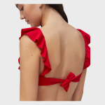 Back view of a model wearing a red one-piece swimsuit featuring shoulder ruffles and a knotted tie-back closure on a white background.