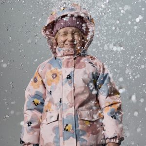 Child wearing pink floral-patterned hooded puffer jacket with snap closures, two front flap pockets, and ribbed cuffs, photographed against gray backdrop with water splashing around.