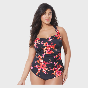 Plus-size model wearing a black one-piece swimsuit with red and pink floral print, halter neckline and gathered waist detailing, front view in studio setting.