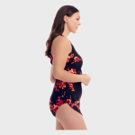 Side view of a woman modeling a black one-piece swimsuit with a vibrant red, pink, and orange floral pattern, shown against a white studio background.
