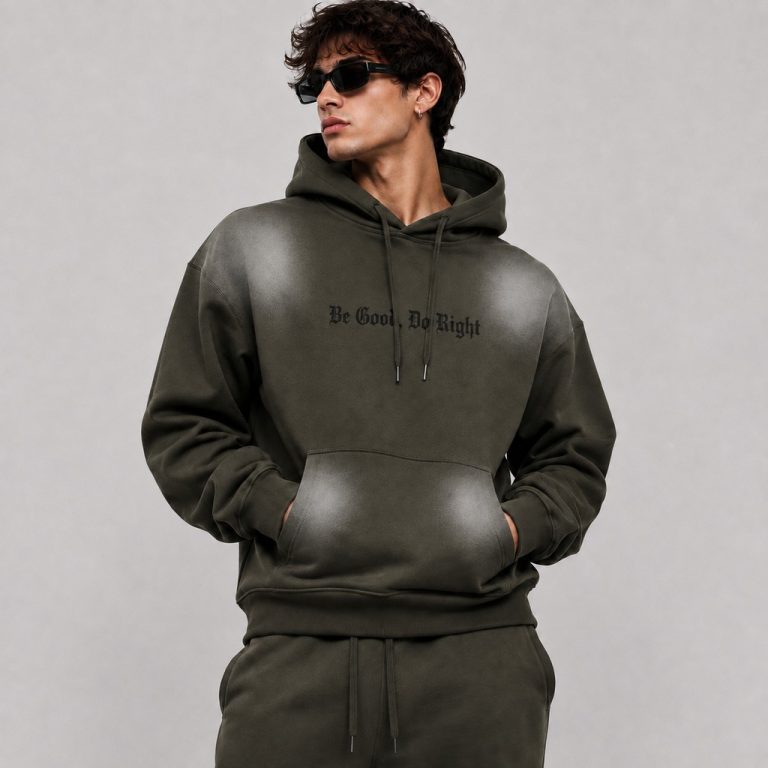 Men's olive green pullover hoodie with spray-print faded effect on shoulders and kangaroo pocket, "Be Good Do Right" gothic text printed in black on the chest center, drawcord hood, ribbed cuffs and hem, model front view wearing sunglasses, matching sweatpants