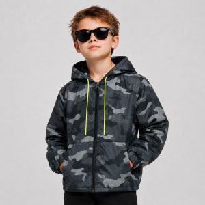 Boy's dark gray black and white abstract geometric halftone camo print hooded windbreaker with full-length silver metal zipper, neon yellow green drawstring on hood, two slanted side pockets, ribbed elasticated cuffs, toggle hem drawcord, kid model front view wearing hood up, black sunglasses, no text or logo