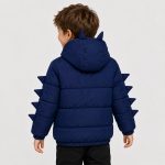Boy's navy blue puffer jacket with hood featuring two 3D dinosaur horns on top, full-length silver metal zipper front, two zip pockets at front waist, four 3D triangular fabric dinosaur spikes running down each sleeve outer seam, ribbed cuffs and hem band, kid model front view wearing hood up, smiling, no text or logo