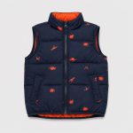 Boy's navy blue puffer vest back view, high funnel collar, allover scattered orange dinosaur silhouette print continuing across back, contrasting orange inner lining, kid model back view brown hair
