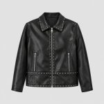Girl's black studded leather (PU faux leather) jacket side three-quarter view, full-length silver metal zipper front, point collar, vertical silver stud line along zipper placket, studded waistband and hem band, two zip pockets visible, kid model wearing heart-shape sunglasses, hair down