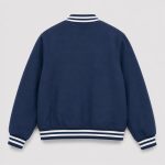 Boy's navy blue classic American varsity letterman bomber jacket flat lay product photo back, ribbed collar cuffs and hem with white double stripe trim, clean plain navy back with no patches or text, clean light gray background for B2B catalog