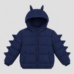 Boy's navy blue puffer jacket flat lay product photo back, hood with two dinosaur horns on top, four 3D triangular fabric dinosaur spikes running down each sleeve outer seam, horizontal quilted construction, ribbed hem, clean light gray background for B2B catalog, no text or logo