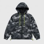 Boy's dark gray black and white abstract geometric halftone camo print hooded windbreaker flat lay product photo back, hood with neon yellow green drawstring, toggle hem drawcord with neon yellow cord ends, ribbed elasticated cuffs, clean light gray background for B2B catalog, no text or logo