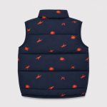 Boy's navy blue puffer vest flat lay product photo back, high funnel collar, allover scattered orange dinosaur silhouette print continuing across back, contrasting orange inner lining edge visible at hem, clean light gray background for B2B catalog, no text or logo