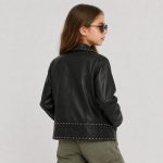 Girl's black studded leather (PU faux leather) jacket flat lay product photo back, point collar, vertical center back seam, studded waistband and hem band, clean light gray background for B2B catalog