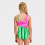 Back view of a child wearing a one-shoulder swimsuit featuring a pink watermelon slice pattern on the top and green vertical stripes on the bottom, with a small bow detail on the shoulder strap.