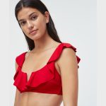 Red bikini-style swim top featuring ruffled shoulder straps and a V-neckline, modeled from a side angle against a plain white studio background.
