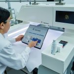 Textile laboratory inspection scene with technician examining fabric label and quality test apparatus.