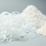Clear plastic bottle flakes beside virgin polyester pellets, showing rPET recycling feedstock.