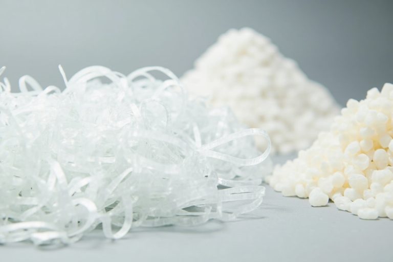 Clear plastic bottle flakes beside virgin polyester pellets, showing rPET recycling feedstock.